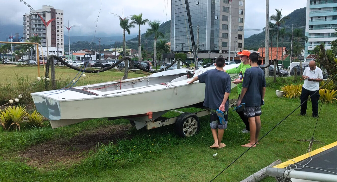 Adolescentes e instrutor ao lado de uma embarcação em área gramada, aprendendo sobre a preparação do barco para navegação.
